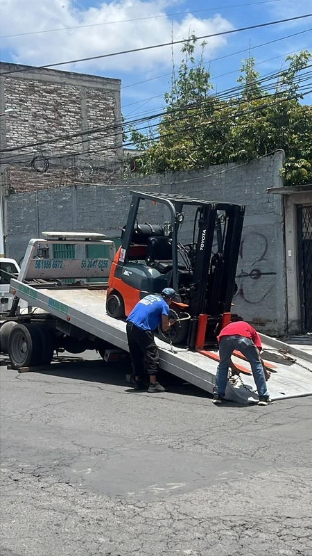 Personal técnico asegurando equipo de carga en plataforma de traslado