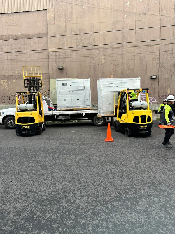 Dos montacargas coordinados descargando equipo industrial con señalización de seguridad